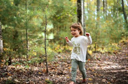 toddler running through woods with NRCM long-sleeved t-shirt