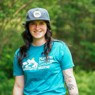 person smiling wearing blue NRCM cap and teal NRCM tee