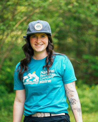 person smiling wearing blue NRCM cap and teal NRCM tee
